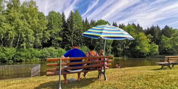 Badeteich mit Familie auf einer Bank mit Sonnenschirm